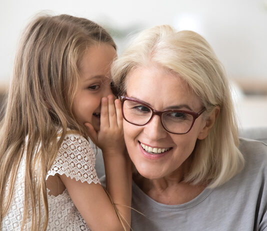 Cute Little Granddaughter Whispering In Ear Telling Secret To Grandma