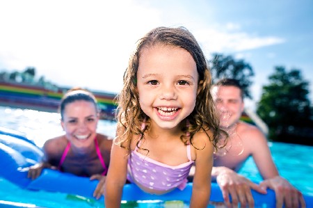 Mother, Father And Daughter In Swimming Pool. Sunny Summer.