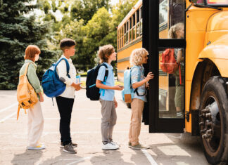 Multiethnic Mixed Race Pupils Classmates Schoolchildren Students Standing In Line Waiting For Boarding School Bus Before Starting New Educational Semester Year After Summer Holidays