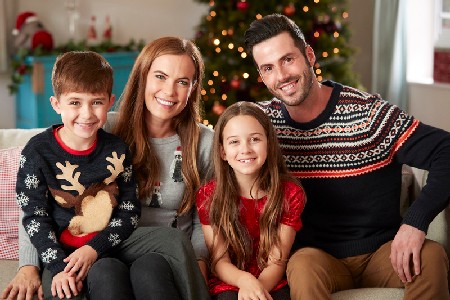 Portrait Of Parents With Children Wearing Festive Jumpers Sitting On Sofa In Lounge At Home On Christmas Day