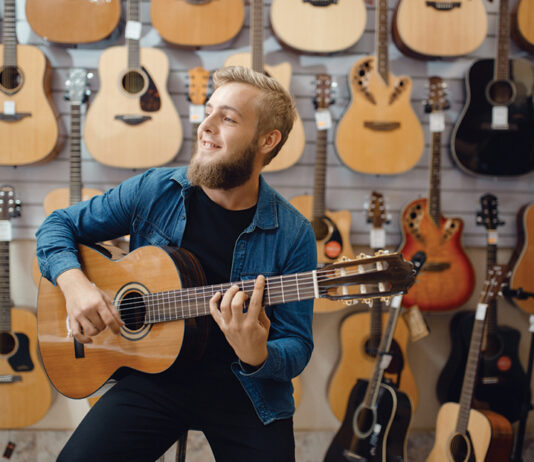 Young Man Plays On Acoustic Guitar In Music Store