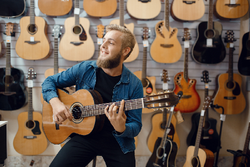 Young Man Plays On Acoustic Guitar In Music Store